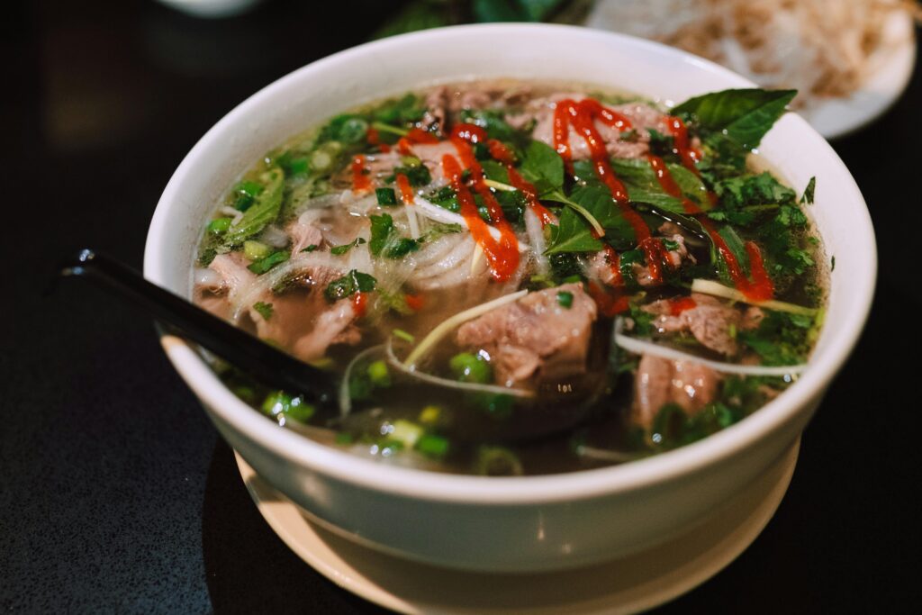 Delicious bowl of traditional Vietnamese pho garnished with fresh herbs and spicy sauce.